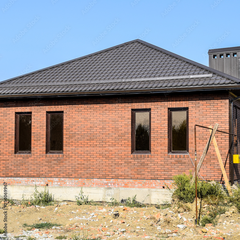 The house with plastic windows and a roof of corrugated sheet. Brown roof and brown brick