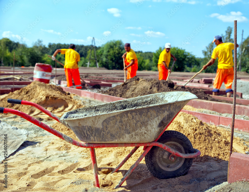 Wheelbarrow with concrete on a construction site, workers in uniform ...
