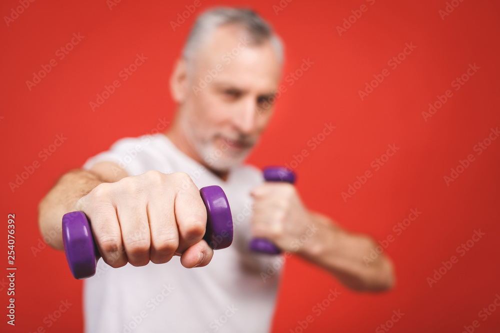 Close-up portrait Of A Senior Man Exercising with dumbbells against red Background. Close-up portrait Of A Senior Man Exercising with dumbbells against red Background.