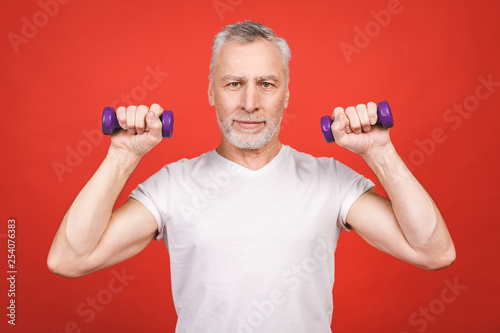 Portrait Of A Senior Man Exercising with dumbbells against red Background.