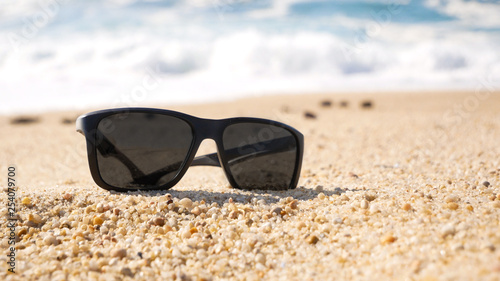 Close up of sunglasses on a sandy beach in summer. Shallow focus.