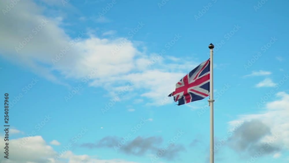 Old Ripped Union Jack Flag Blowing in Slow Motion Against Blue Sky Old Ripped Union Jack Flag Blowing in Slow Motion Against Blue Sky