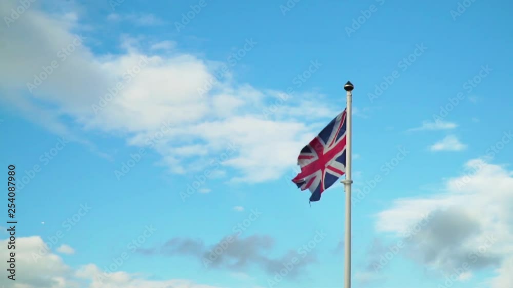Tattered Union Jack Flag Blowing in Slow Motion Against Blue Sky Tattered Union Jack Flag Blowing in Slow Motion Against Blue Sky