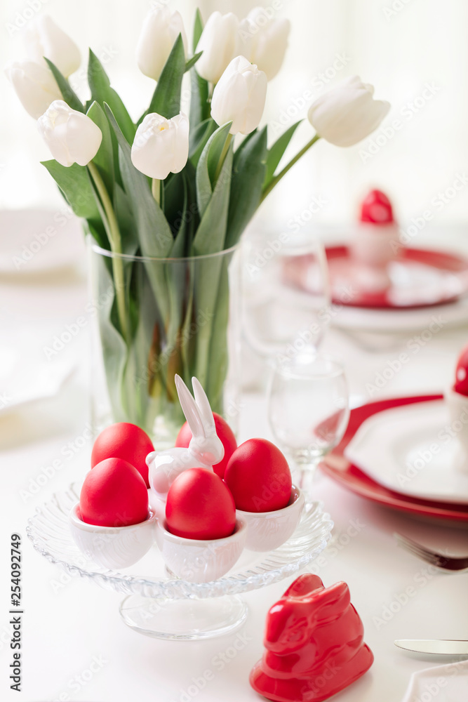 Happy easter. Decor and table setting of the Easter table is a vase with white tulips and dishes of red and white color. Easter colored eggs with white polka dots.