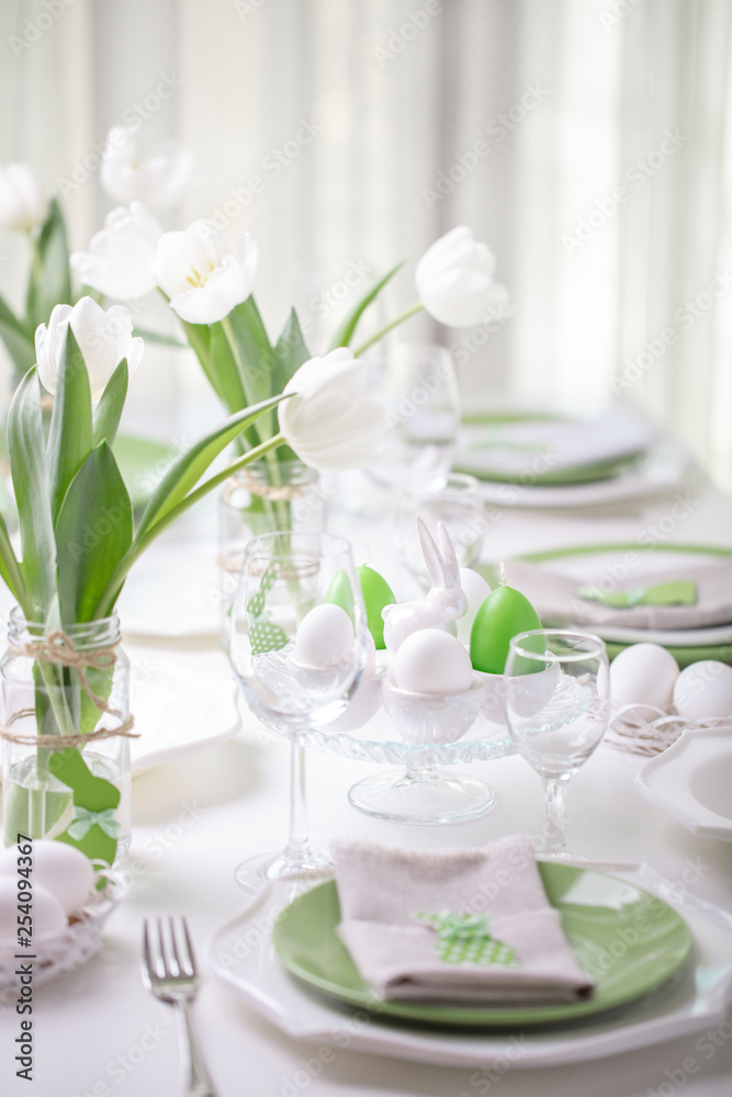 Decor and table setting of the Easter table with white tulips and dishes of green and white color. Easter decor in the form of Easter bunnies green color with white polka dots. Decor and table setting of the Easter table with white tulips and dishes of green and white color. Easter decor in the form of Easter bunnies green color with white polka dots.