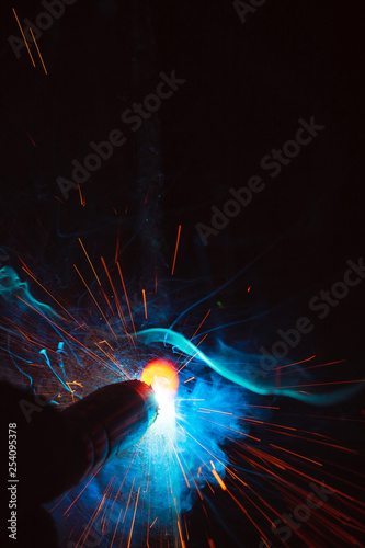 Arc welding. Welding of two metal plates in inert gases. MIG / MAG. A bright flash of light and a sheaf of sparks.