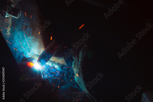 Arc welding. Welding of two metal plates in inert gases. MIG / MAG. A bright flash of light and a sheaf of sparks.