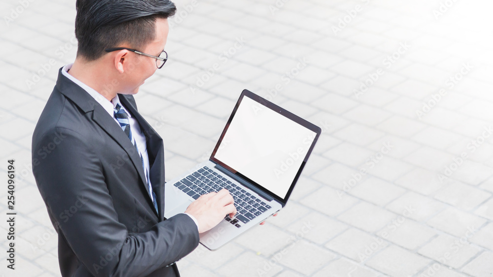 Asian Smart Businessman standing and working with laptop with blank white screen.Concept of business people using technology. Asian Smart Businessman standing and working with laptop with blank white screen.Concept of business people using technology.