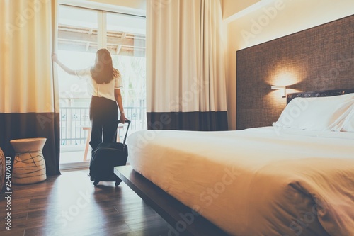 Asian women are staying in a hotel room. Open the curtain in the room Along with carrying luggage.Concept of people be comfortable to travel.