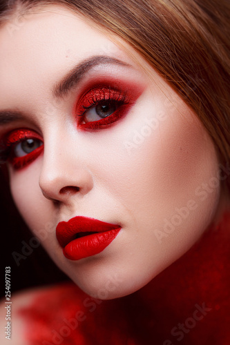 Red makeup in the style of beauty. Bright lips and eyes. Portrait of a beautiful young girl. Journal detailed skin retouching. Expressive eyebrows. Huge eyelashes. Neon shadows.