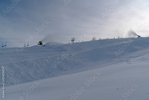 Snow covered slope with snow cannons and ski lifts