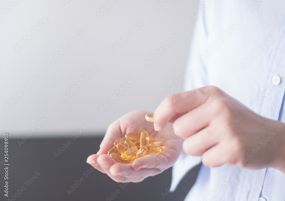 Obraz premium Healthy eating and diet nutrition concepts. vitamin and supplement. beautiful young woman holding yellow fish oil pill. female hand putting omega-3 capsule in mouth.