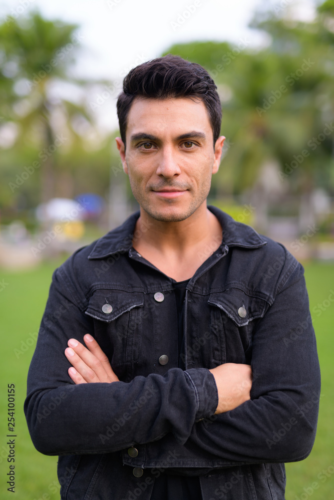 Young handsome Hispanic man with arms crossed in the park outdoors Young handsome Hispanic man with arms crossed in the park outdoors
