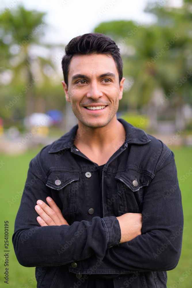 Young happy Hispanic man smiling with arms crossed in the park Young happy Hispanic man smiling with arms crossed in the park