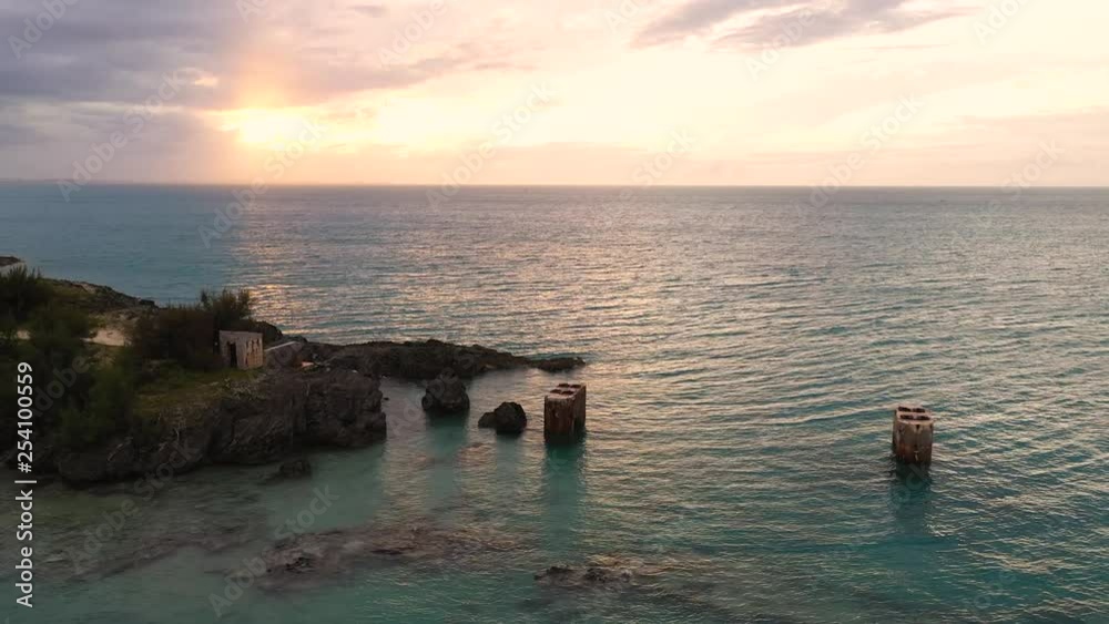 Aerial view of old bridge mounts in clear turquoise water by tropical island. Sunset over big ocean. PULLBACK.