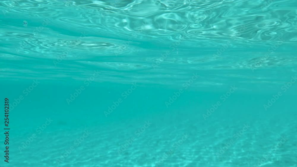 SLOW MOTION, UNDERWATER, DOF: Glassy surface of the exotic sea glimmers in the summer sunlight. Spectacular underwater view of the endless turquoise sea water and white sand seabed of the Caribbean. SLOW MOTION, UNDERWATER, DOF: Glassy surface of the exotic sea glimmers in the summer sunlight. Spectacular underwater view of the endless turquoise sea water and white sand seabed of the Caribbean.