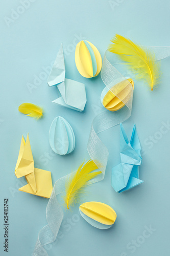 Easter holiday creative background with papercraft eggs, origami bunny on pastel blue table, trendy paper craft holiday background, top view, copy space