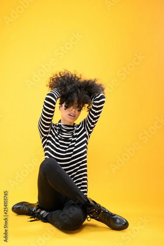 Young Black Woman in a Stripped Shirt sitting on a yellow background