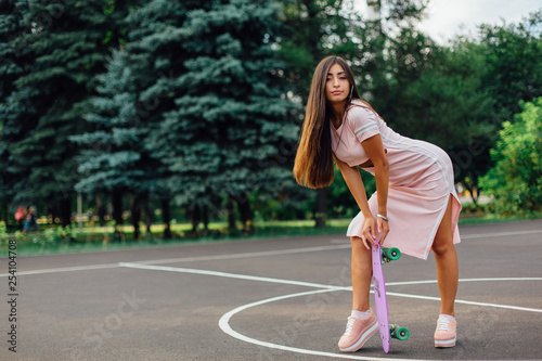Portrait of a smiling charming brunette female holding her skateboard on a basketball court.