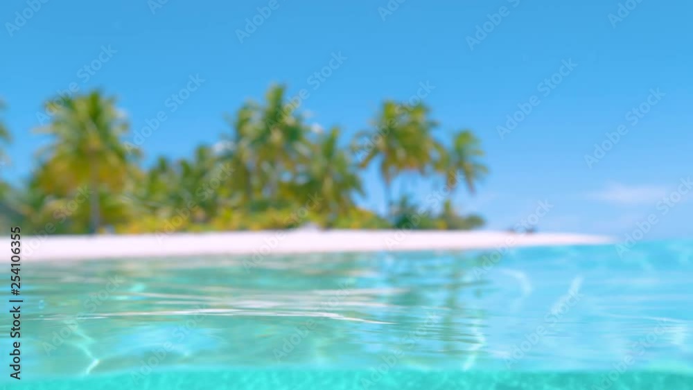 SLOW MOTION, HALF UNDERWATER, DOF Spectacular jewel colored water and the untouched white sand tropical beach under the sunny sky. Idyllic exotic island in the Pacific is surrounded by turquoise water