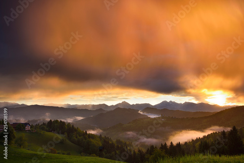 Golden sunrise in the mountains of Kamnik Savinja Alps and rolling fog in Skofjelosko Hills with St Thomas church near Ljubljana Slovenia