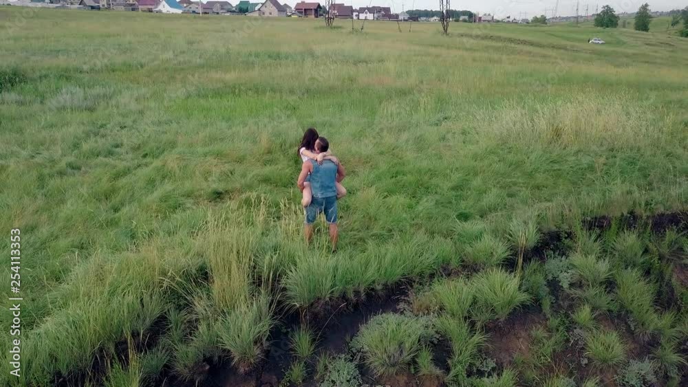wonderful upper view brunette girl in white t-shirt and denim shorts jumps into man arms on green meadow wonderful upper view brunette girl in white t-shirt and denim shorts jumps into man arms on green meadow