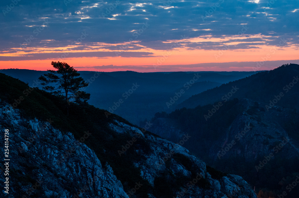 Obraz premium bright red dawn in the mountains in a windy, cloudy morning, the sun rises from the horizon