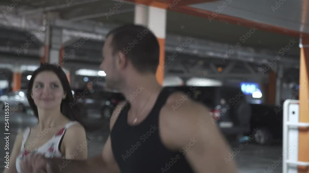 young couple in summer dressing runs in underground parking lot with orange and blue columns young couple in summer dressing runs in underground parking lot with orange and blue columns