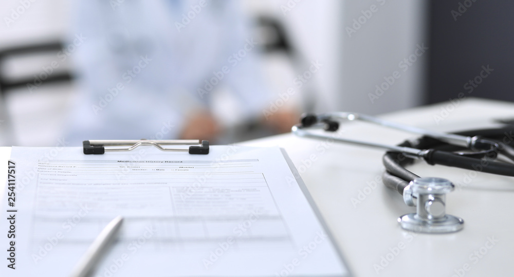 Stethoscope, clipboard with medical form lying on hospital reception desk with laptop computer. Medical tools at doctor working table.Medicine and health care concept Stethoscope, clipboard with medical form lying on hospital reception desk with laptop computer. Medical tools at doctor working table.Medicine and health care concept
