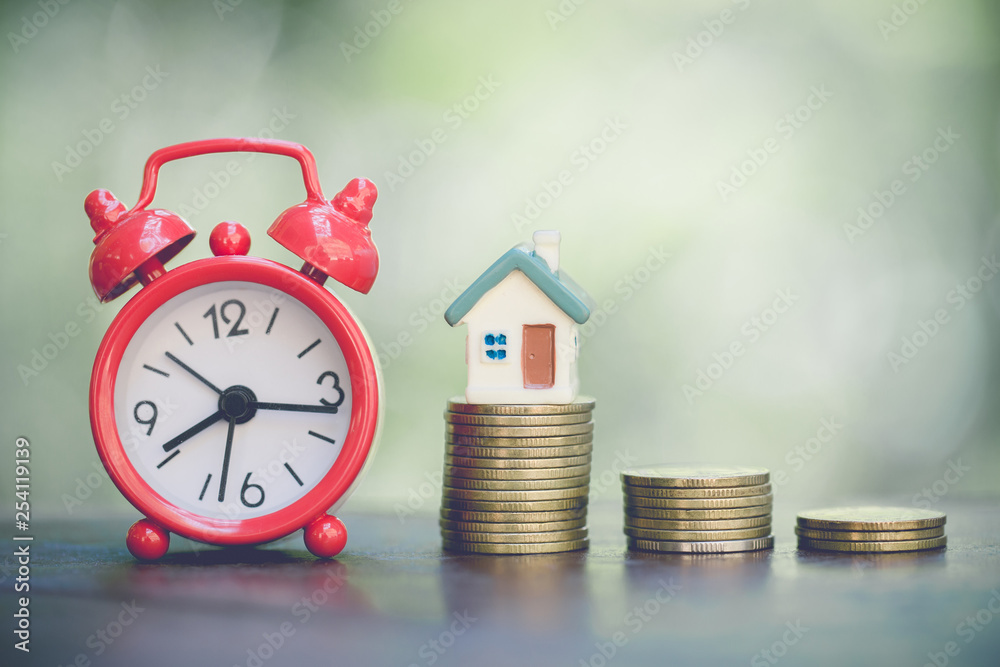 pile of money coins growing up with house model and alarm clock concept in business about loan sellingfinance mortgage and buying home, Vintage tone. pile of money coins growing up with house model and alarm clock concept in business about loan sellingfinance mortgage and buying home, Vintage tone.