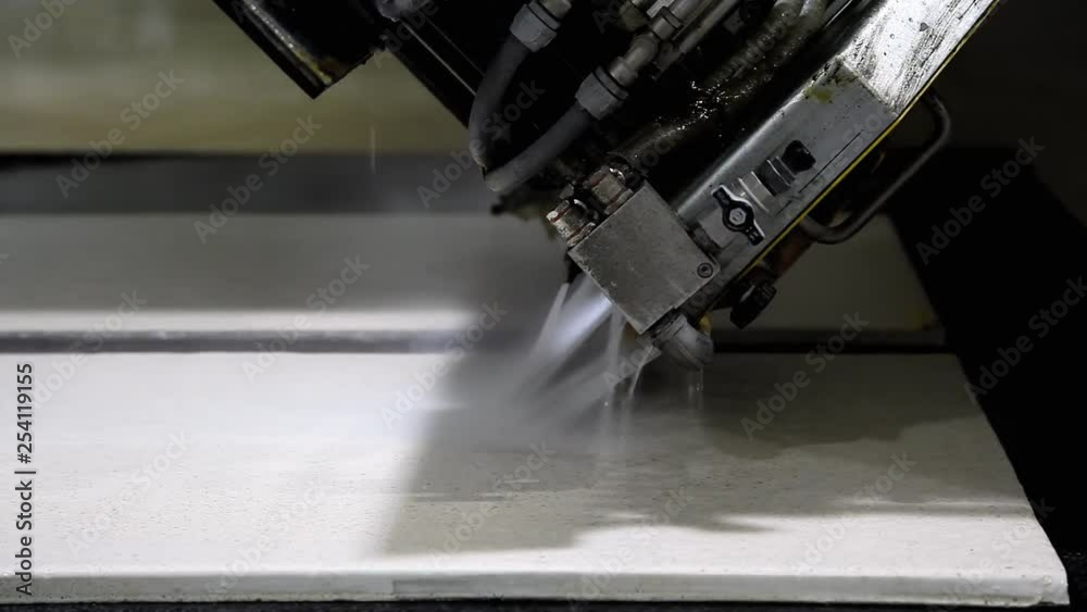 The operations of a cutting bench at a countertop factory: an automated machine saw starting to engrave an angled line on a heavy granite block, while releasing a flow of cooling water. The operations of a cutting bench at a countertop factory: an automated machine saw starting to engrave an angled line on a heavy granite block, while releasing a flow of cooling water.