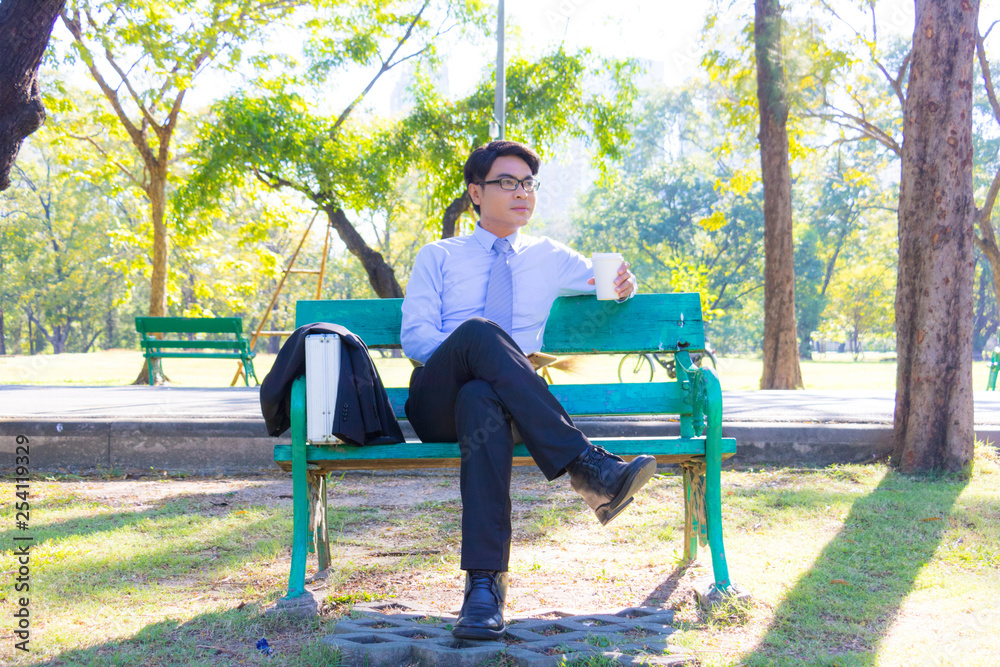 Businessman, He is sitting on bench in park. He is thinking about business. He is drinking coffee beside business bag. Photo concept  business and relax time.