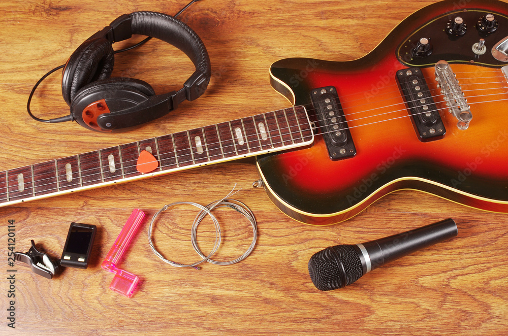 Naklejka premium Electric guitar, microphone, headphones, strings on a wooden table.