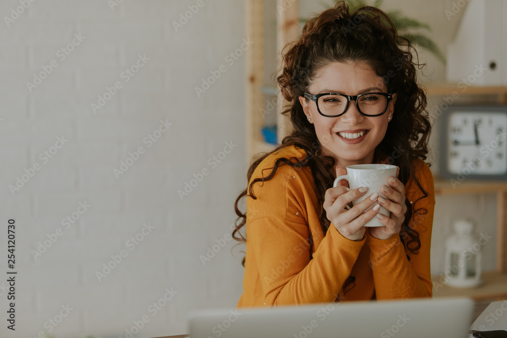 Portrait of a beautiful curly brunette in glasses, holding her coffee mug. Looking at camera, smiling. Image with negative space. Portrait of a beautiful curly brunette in glasses, holding her coffee mug. Looking at camera, smiling. Image with negative space.