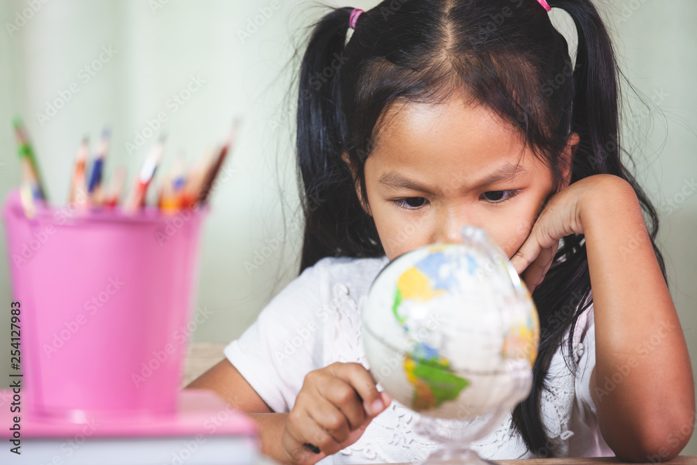 Cute asian child girl use magnifier to look and study at the globe in classroom Cute asian child girl use magnifier to look and study at the globe in classroom
