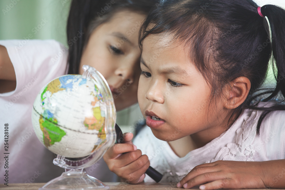 Two cute asian child girls use magnifier to look and study at the globe together in classroom Two cute asian child girls use magnifier to look and study at the globe together in classroom