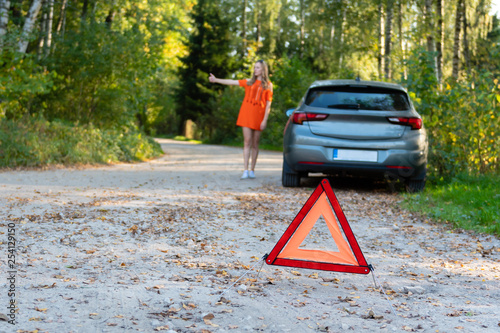 Stressful young woman driver hitchhikes and stops cars, asks for help as have problem with brocken car, uses red triangle sign to warn drivers about stop. (selective focus)