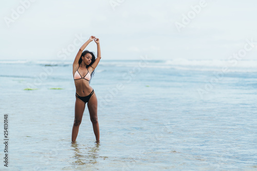 Beautiful dark skinned girl in swimwear resting on beach. African american model posing on tropical island