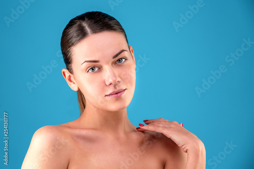 Close up Beauty portrait of young woman brunette smiling and touching her face on blue background. Perfect Fresh Skin. Youth and Skin Care Concept.