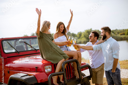 Young people drinking and having fun by car outdoor at hot summer day