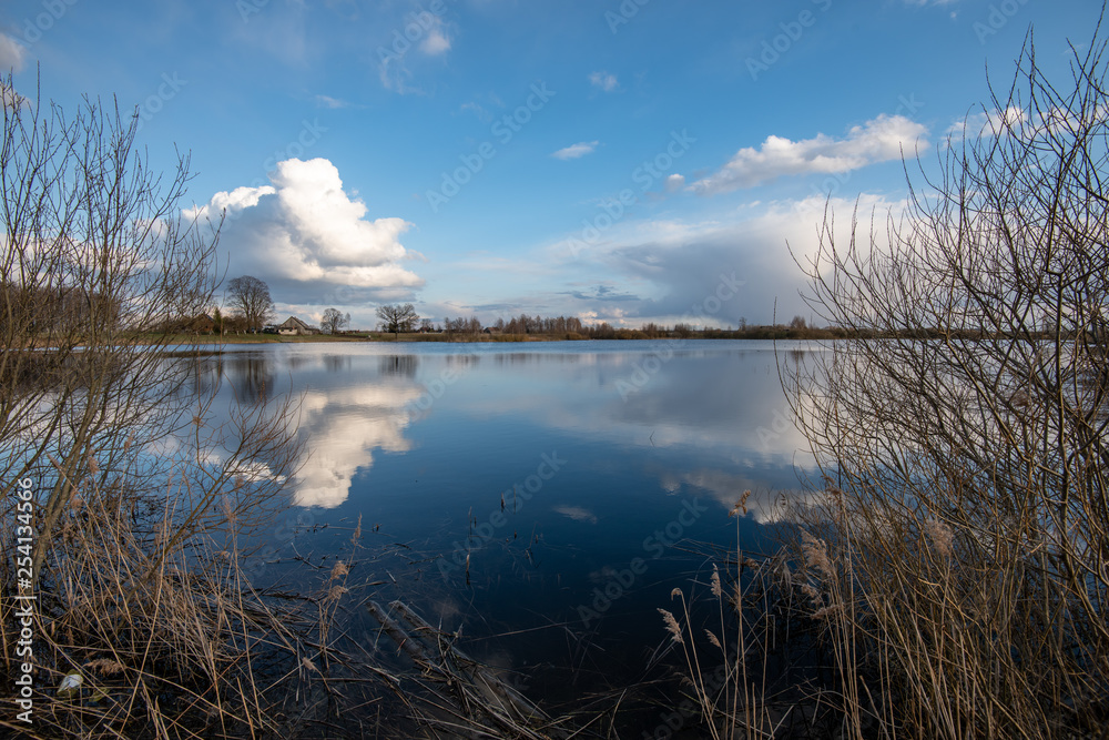 Fototapeta premium calm lake in bright sun light with reflections of clouds and trees and blue sky