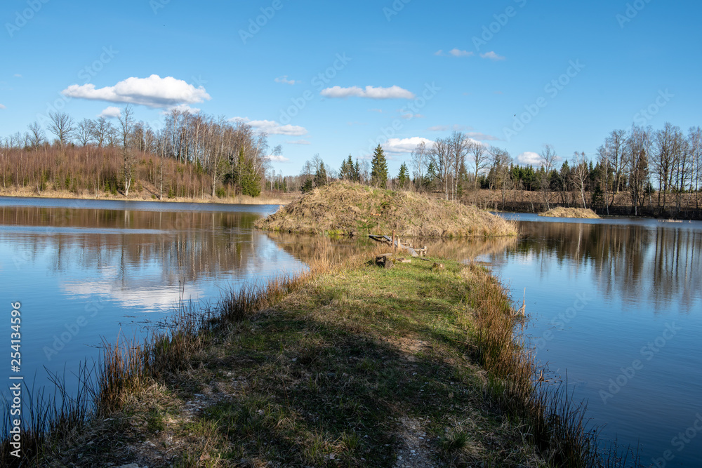 calm lake in bright sun light with reflections of clouds and trees and blue sky calm lake in bright sun light with reflections of clouds and trees and blue sky