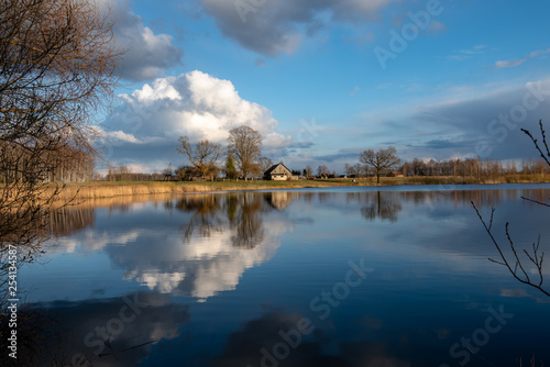 calm lake in bright sun light with reflections of clouds and trees and blue sky