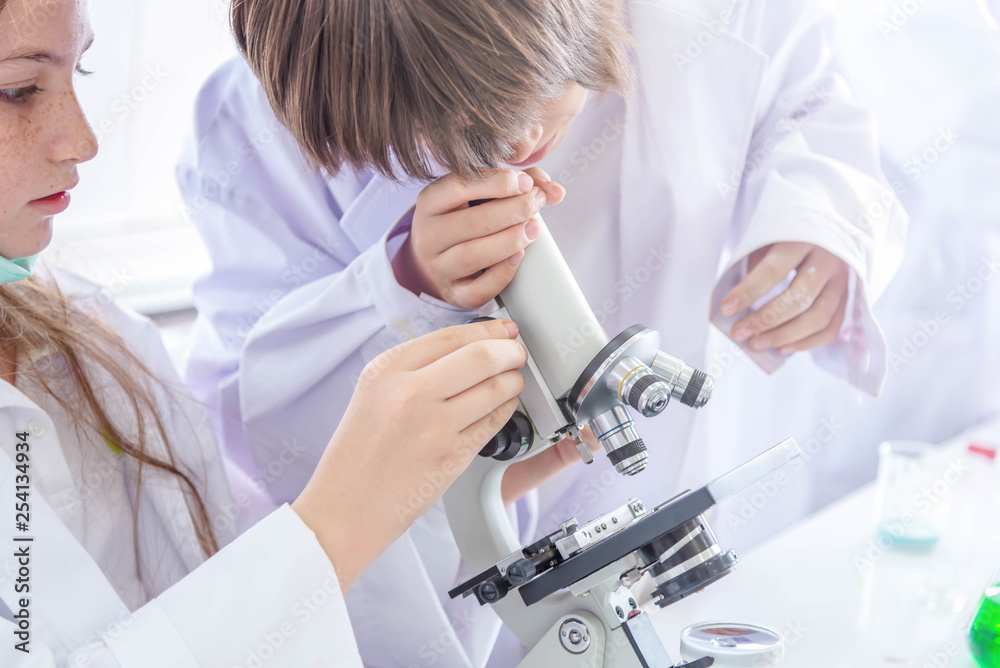 Student learning chemistry. Positive joyful smart boy and girl tesing and using a microscope in science class. Two children help each other in class. Student learning chemistry. Positive joyful smart boy and girl tesing and using a microscope in science class. Two children help each other in class.