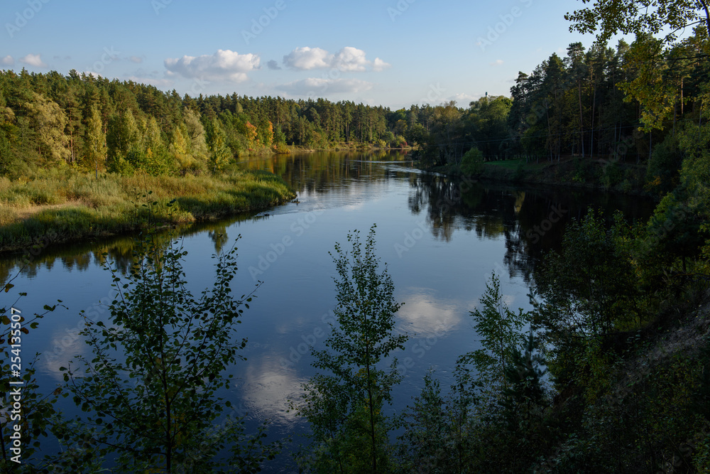 calm lake in bright sun light with reflections of clouds and trees and blue sky