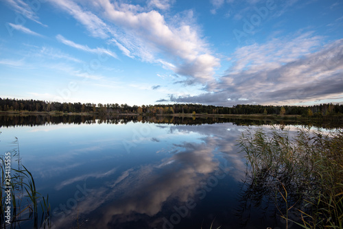 calm lake in bright sun light with reflections of clouds and trees and blue sky