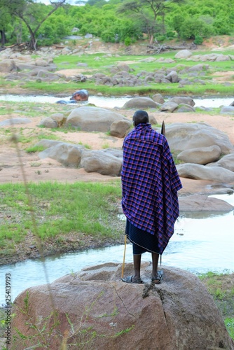 Masái con su tunica azul mirando a un hipopotamo a lo lejos en el río Ruaha en el Parque Nacional de Ruaha en Tanzania, Africa del Este