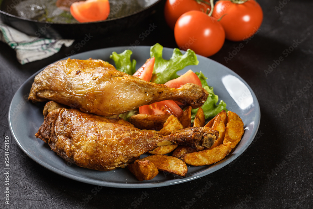 Roasted chicken legs with potato wedges and tomatoes