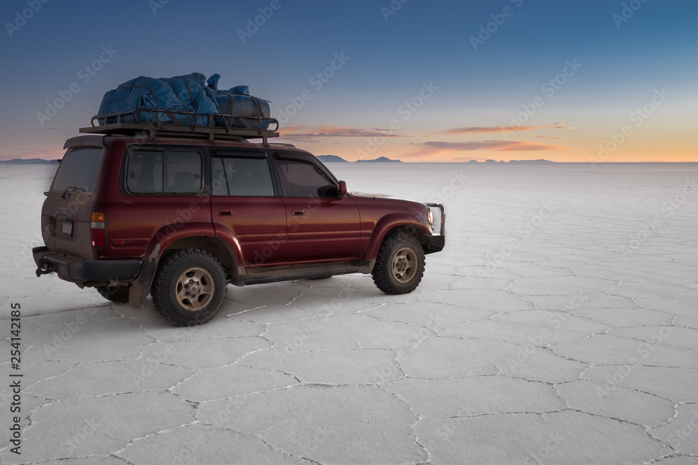 A tour 4x4 car sits on the amazing white vast landscape of the largest salt plain in the world at Salar De Uyuni (Salt Flat), Bolivia with the cactus island in the distance