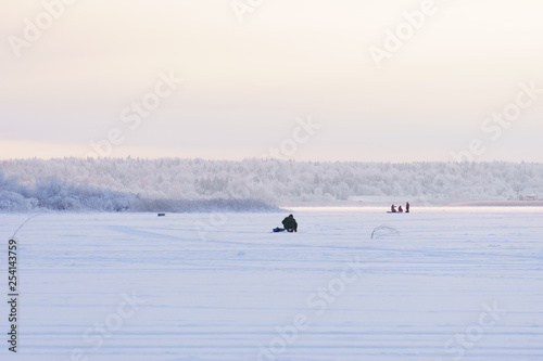 Fisherman fishes on the lake in winter  sunset